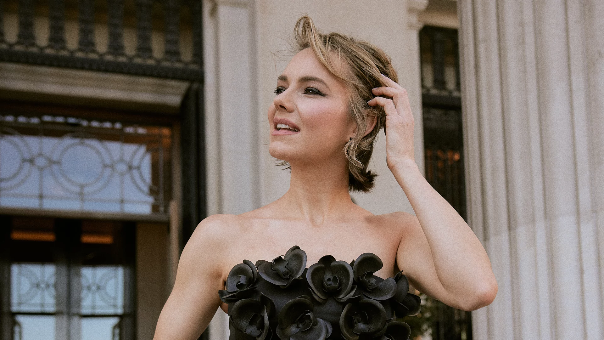 Kara Tointon Black Dress Red Carpet Event Hero Close up of actress Kara Tointon holding up her hand to her hair on the red carpet.